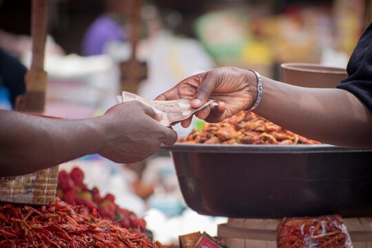 Two African hands of a seller and buyer exchanging money, cash, currency or naira notes in a market place during transaction