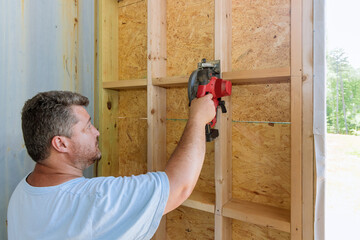 Building contractor worker using hand electric circular saw to cut wooden plank boards on a new home construction