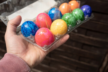 Fototapeta na wymiar Male hand holds a transparent tray with bright colored Easter eggs, against the background of a black table. 
