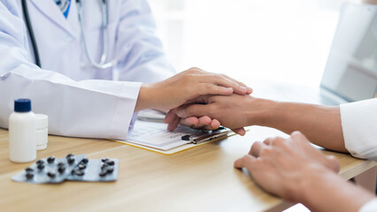 Fototapeta premium Visiting a doctor concept A doctor giving his support to the patient and making it certain by putting his hand and the patient’s hand together.