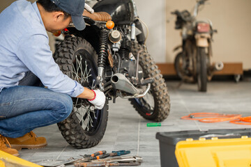 Young man fixing motorcycle in workshop garage, Man repairing motorcycle in repair shop, Mechanical...