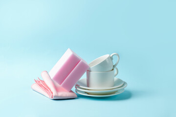 Set of pink sponges and white cups on blue background, kitchenware, house cleaning service concept, copy space, banner, flyer, mockup, minimal design