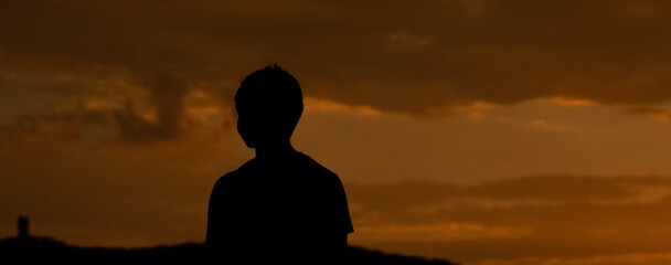 Panoramic silhouette shot of an Indian kid looking at the orange sky during the sunset. Hopeful kid...