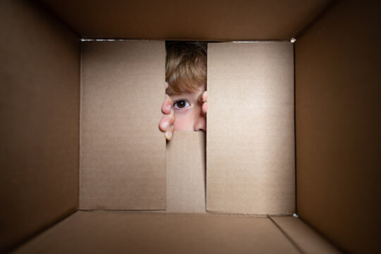 Happy little child boy is opening gift and looking inside cardboard box. Close up eyes looking.