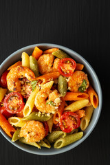 Homemade Tri-Color Penne Salad with Shrimp, Tomato and Basil Bread Crumbs in a Bowl on a black background, top view. Flat lay, overhead, from above.