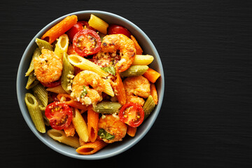 Homemade Tri-Color Penne Salad with Shrimp, Tomato and Basil Bread Crumbs in a Bowl on a black background, top view. Flat lay, overhead, from above. Copy space.
