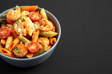 Homemade Tri-Color Penne Salad with Shrimp, Tomato and Basil Bread Crumbs in a Bowl on a black background, side view.