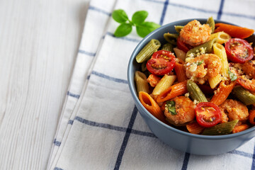 Homemade Tri-Color Penne Salad with Shrimp, Tomato and Basil Bread Crumbs in a Bowl on a white wooden background, side view. Copy space.