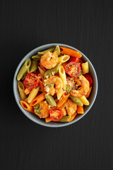 Homemade Tri-Color Penne Salad with Shrimp, Tomato and Basil Bread Crumbs in a Bowl on a black background, top view. Flat lay, overhead, from above.
