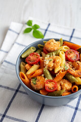 Homemade Tri-Color Penne Salad with Shrimp, Tomato and Basil Bread Crumbs in a Bowl on a white wooden background, side view.