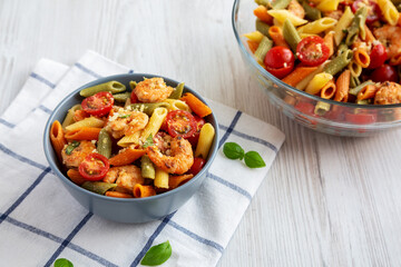 Homemade Tri-Color Penne Salad with Shrimp, Tomato and Basil Bread Crumbs in a Bowl on a white wooden background, side view.