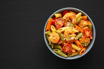 Homemade Tri-Color Penne Salad with Shrimp, Tomato and Basil Bread Crumbs in a Bowl on a black background, top view. Flat lay, overhead, from above. Copy space.