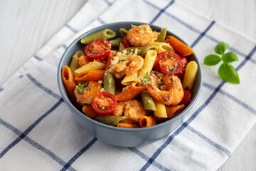 Homemade Tri-Color Penne Salad with Shrimp, Tomato and Basil Bread Crumbs in a Bowl on a white wooden background, side view.