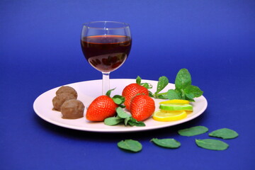 On a plate, a glass of red wine, red strawberries, chocolates, lemon wedges. Red cherry. Romantic...