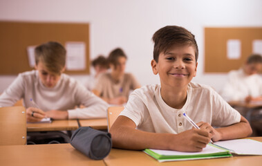 Portrait of positive teenage schoolgirl sitting on lesson in classroom