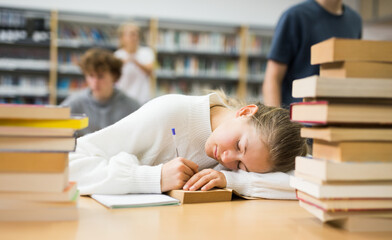Portrait of a tired fourteen-year-old schoolgirl who fell asleep on a desk among textbooks in the...