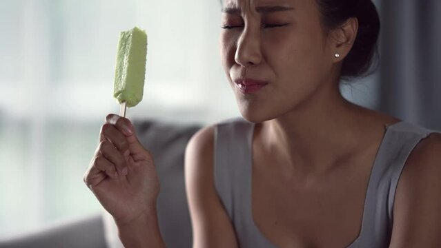 Young Asian woman have sensitive teeth with ice. Woman eating ice cream have toothache. Healthcare concept.