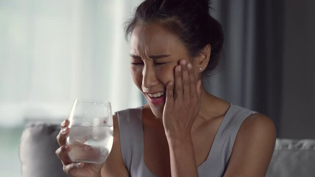 Young Asian woman have toothache while drinking water with ice from glass. Health care concept.