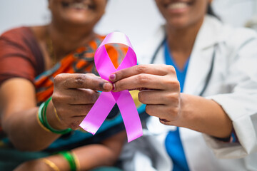 close up shot of doctor and patient showing breast cancer symbol by to camera at hospital - concept...