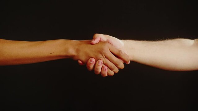 Diverse people making handshake gesture isolated on black background. International friends holding hands, hand clasp close-up, clapping.