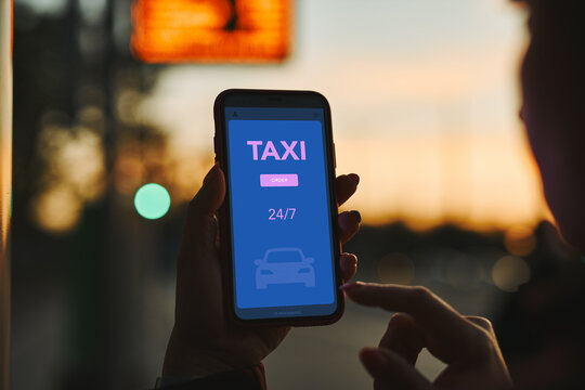 Woman ordering taxi online using mobile app on smart phone. Booking taxi using application online. Arranging taxi ride in downtown city street. Car sharing. Taxi service on mobile