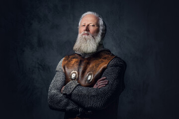 Shot of gray haired medieval soldier dressed in armored clothes posing against dark background.
