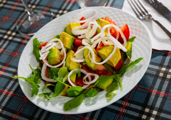 Healthy vegan salad with avocado, arugula and tomato on a white plate