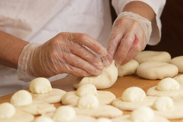 Obraz na płótnie Canvas Baker makes filled pies from yeast dough. Hands in protective gloves wraps the curd filling into the yeast dough. Work in bakery. Selective focus.