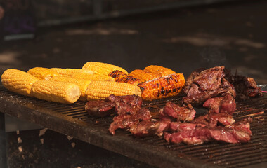 Grilling corn cobs and meat on a large outdoor grill at Prague farmers street food market.