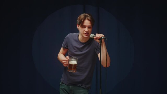 Drunk man singing on stage and drinking beer. Young guy in karaoke, male person speaking with audience using microphone.