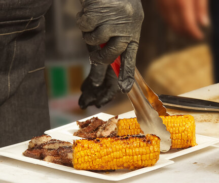 Chef serves portions of grilled meat and corn on the cob