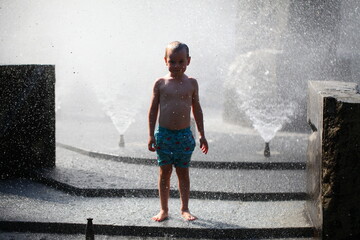 Fototapeta na wymiar child boy playing in the park in the spray of the fountain