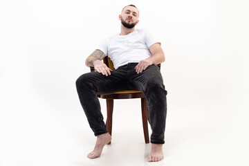 Tattooed handsome brunet, confident, bearded barefoot man sit relaxing like boss on chair like boss. Low angle view