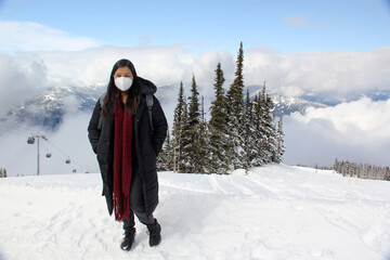 Latin adult woman arrives in Canada and discovers the snowy mountains with a face mask due to the...