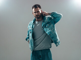 Portrait of handsome confident stylish hipster lambersexual model. Sexy man dressed in jeans jacket. Fashion male isolated on grey background in studio