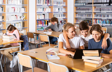 Smart teenagers spending time in library together and doing their homework. Some of them using laptop.