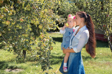 Happy smiling mom with a daughter childwalking in the apple orchard on a sunny summer day. Mother and girl kid in Issyk Kul Lake, Kyrgyzstan . Happy family