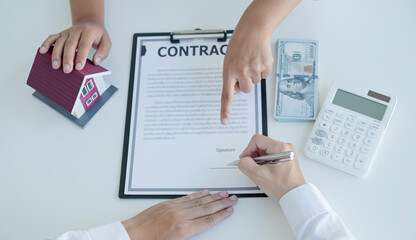 A real estate agent with a house model is talking to clients about buying home insurance and having customers sign contracts under the formal contract agreement. Home rental and insurance concept