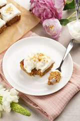 Homemade pastry carrot-walnut cake with grounded almonds and hazelnuts and white cream cheese top layer on white plate on pink napkin