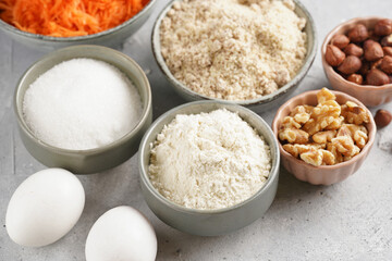 Ingredients for baking a carrot cake: finely grated carrots, grounded hazelnuts and almonds, chopped walnuts, white flour, eggs, sugar on grey background