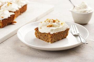 Homemade pastry carrot-walnut cake with grounded almonds and hazelnuts and white cream cheese top layer on white plate