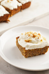 Homemade pastry carrot-walnut cake with grounded almonds and hazelnuts and white cream cheese top layer on white plate