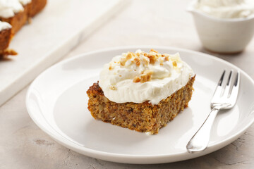 Homemade pastry carrot-walnut cake with grounded almonds and hazelnuts and white cream cheese top layer on white plate