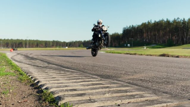 Stunt motorcycle rider performing wheelie ride on one wheel in race track