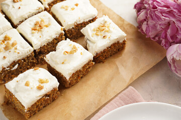 Homemade pastry carrot-walnut cake with grounded almonds and hazelnuts and white cream cheese top layer: several cut pieces on parchment paper