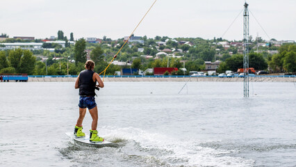 A young woman on the lake is engaged in wakeboarding. A city in the blurry background. Active...