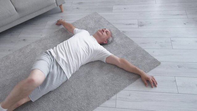 Pilates exercise. Home fitness. Strength flexibility. Health wellbeing. Relaxed middle-aged man stretching back lying on floor on carpet.