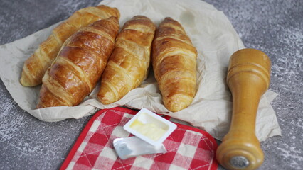 A pile of delicious fresh croissants served with butter on a gray table.