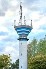 White brick water tower with wireless communication antenna transmitter against blue sky and trees.Internet, 3G, 4G and 5G cellular connection.