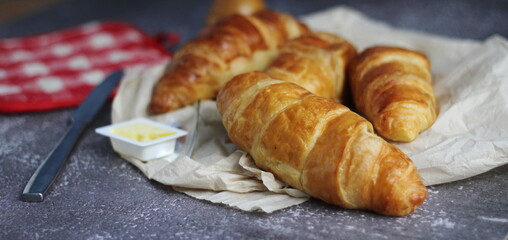 A pile of delicious fresh croissants served with butter. On a gray table with a blue background.